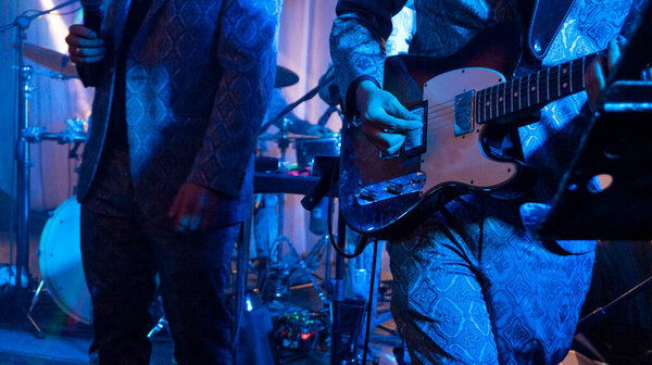 Close up view of guitarist in blue suit playing during a concert at night