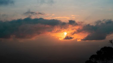 Gün batımının panoramik manzarası. Güneş bulutların arasında batıyor. Ağaçların siyah siluetleriyle.