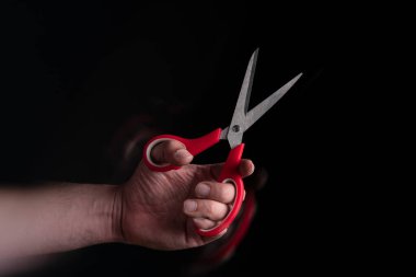 Siyah arkaplana karşı hareket etkisine sahip kırmızı saplı makas tutan adamın elini kapat
