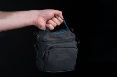 Siyah arka planda mavi olan küçük siyah bavulu tutan adamın elini kapat.