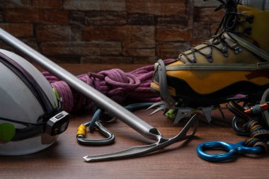 Tırmanma ekipmanları, halat, karabinalar, buz baltası, far ile kask, duvarda krampon olan botlar olan tahta masa ön görünümü.