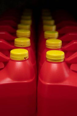 Kırmızı plastik motor yağı şişelerinden oluşan iki sütunun ön görüntüsü, saplı bir kap ve koyu arka planda etiketsiz sarı vida kapağı