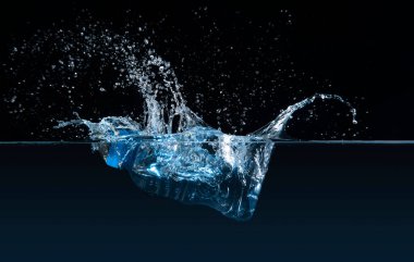 Suya batırılmış temiz plastik şişenin ön görüntüsü siyah arka planda bir sıçramaya neden oluyor.