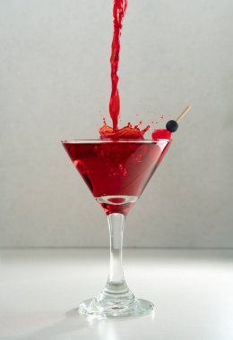 Kırmızı içkinin seramik masadaki konik bardakta gri arka planda vişne kokteyle sıçrayan akımının ön görüntüsü.