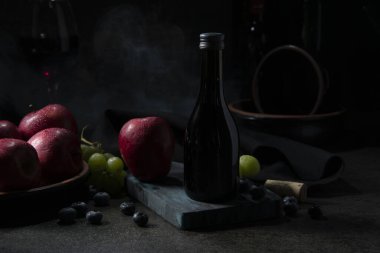 Kırmızı elmaların, yeşil üzümlerin ve siyah seramik bir masanın üzerinde siyah bir bezle doğranmış yaban mersinlerinin yanında bir şişe şarap.