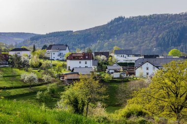 Yeşil tepelerin ve çiçek açan ağaçların arasına yuva yapmış evlerle dolu ideal kırsal alan.