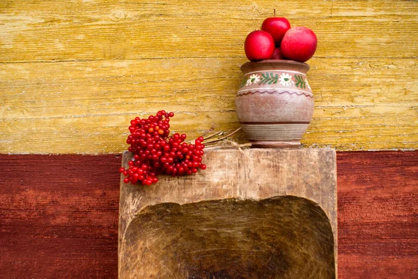 Elmalı kil çömlek ve ahşap bir yalağın üzerinde viburnum dalı, bir sonbahar günü eski bir ahşap evin arka planına karşı
