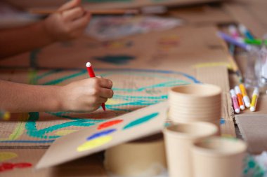 Kahverengi geri dönüşümlü karton üzerine kırmızı işaretli küçük bir çocuğun el çizimi.