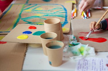 Kahverengi geri dönüşümlü karton üzerinde yeşil, sarı, kırmızı suluboya çocuk resimleri.