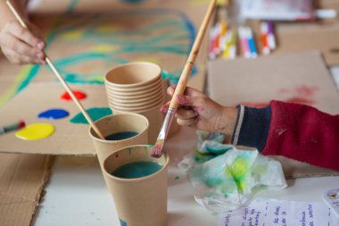 Kahverengi geri dönüşümlü karton üzerinde fırça ve suluboya ile küçük bir çocuğun el çizimi
