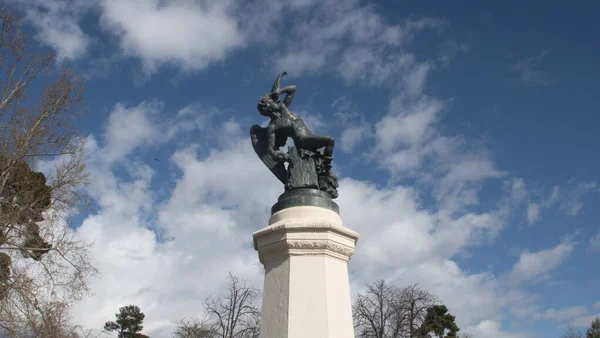stock image Statue of a person representing the Fallen Angel in black with wings and a snake on a pedestal of gray granite in the Retiro Park in Madrid.