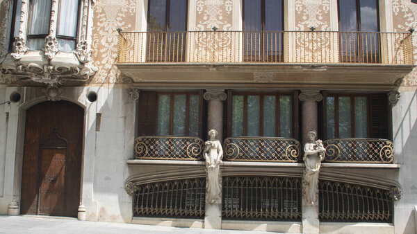 Restored facade of an old building in the center of the city of Olot in Catalonia. Ornamental drawings on facade. Glass windows. Columns and stone statue.