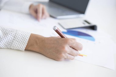 Bilgisayarı ve hesap makinesiyle finansal istatistikler üzerinde çalışan beyaz gömlekli orta yaşlı bir kadının elleri