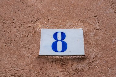 Eski duvarda kare beyaz seramik tuğla ve mavi renkte sekiz numara.