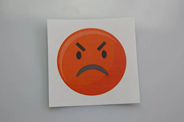 Square piece of paper with the face of an angry emoji