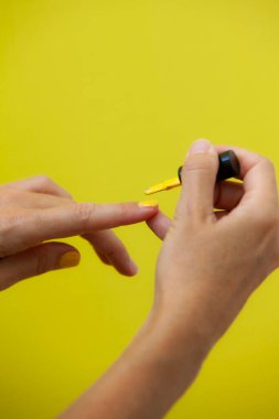 Sarı arka plana tırnaklarını boyayan bir kadının dikey fotoğrafı..