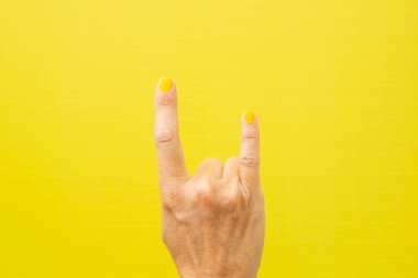 Tırnakları sarıya boyanmış tipik ağır metal boynuzları yapan bir kadının yatay fotoğrafı..