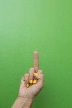 Tırnakları yeşil arka planda sarıya boyanmış bir kadının parmağı orta parmağını hakaret işareti olarak gösteriyor..
