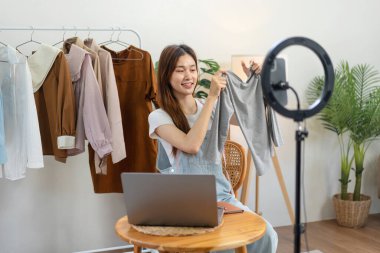 Kadın çevrimiçi satıcı, yeni modalar tanıtmak ve müşteriyle sosyal medyada çevrimiçi kıyafet satmak için konuşurken akıllı telefonu kullanarak Vlog 'ta canlı yayın yapıyor..