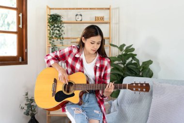 Genç kadın, evdeki oturma odasında dinlenirken şarkı söylemek ve pop şarkılarıyla gitar çalmak için temel gitar akorları çalışıyor..