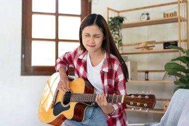 Genç kadın, evdeki oturma odasında dinlenirken şarkı söylemek ve pop şarkılarıyla gitar çalmak için temel gitar akorları çalışıyor..