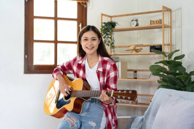 Genç kadın, evdeki oturma odasında dinlenirken şarkı söylemek ve pop şarkılarıyla gitar çalmak için temel gitar akorları çalışıyor..