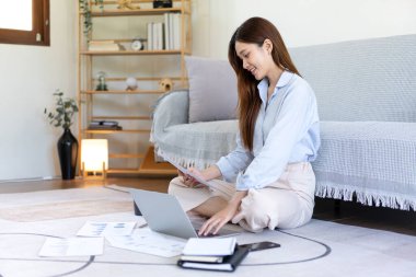 Kadın serbest meslek belgesi okuyor ve yerde otururken ve merkez ofisteki oturma odasında çalışırken dizüstü bilgisayarda bilgi yazıyor..