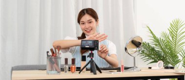 Genç güzellik etkileyicisi, sosyal medyada veya stüdyoda web blogcusu paylaşımı için kameraya video kaydederken ve kozmetik ürünlerini test etmek ve tavsiye etmek için ruj ürünü gösteriyor.