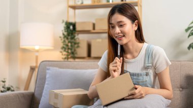 Genç girişimci online siparişleri kontrol etmek için tablet kullanıyor ve karton kutulara müşteri adresleri yazarken aynı zamanda kanepede oturuyor ve ev ofisinin oturma odasında çalışıyor..