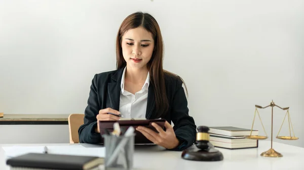 stock image Business lawyer woman is reading business contract and writing data on document while working on the table with brass scales and justice hammer in law firm.