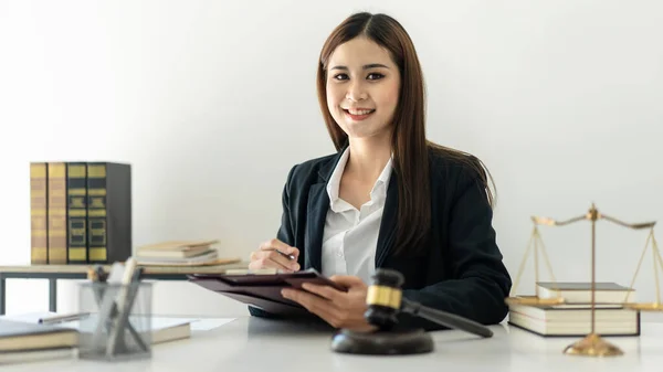 Business lawyer woman is reading business contract and writing data on document while working on the table with brass scales and justice hammer in law firm.