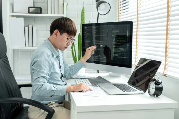 Male programmer is programming to develop program app and website of corporate while working to checking program code and debugging on multiple screen at modern software office.
