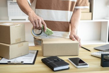 Erkek girişimci ürünleri kontrol ettikten ve akıllı telefondan çevrimiçi sipariş aldıktan sonra merkez büroda çevrimiçi alışveriş yaparken kutulara koyuyor..