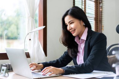 Takım elbiseli genç iş kadını, analiz stratejisi ve ofiste yeni iş planları yapmak için dizüstü bilgisayar kullanıyor..