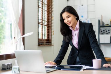 Takım elbiseli genç iş kadını, strateji analizi ve yeni iş planları hakkında çalıştıktan sonra ofiste dizüstü bilgisayarından veri arıyor..