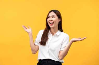 Genç Asyalı bir kadın beyaz kısa kollu gömlek giyer ve gülümserken iki elini de sarı arka planda izole edilmiş bir şeyi tanıtmak ve tanıtmak için açar..