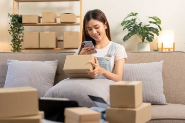 Genç girişimci, müşteri göndermek için karton kutular tutuyor. Bu sırada rahat koltukta oturuyor ve merkez ofisteki oturma odasında çalışıyor..