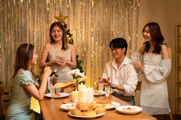 Young people talking and eating dinner together while drinking champagne to celebrate and toasting in holiday of new year party at home.