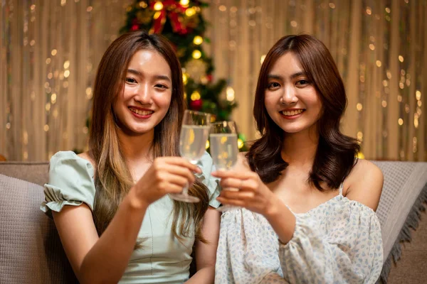 Young beautiful people is sitting on the couch to clinking glass of champagne to toasting with happiness and talking while celebrating together in new year party at home.
