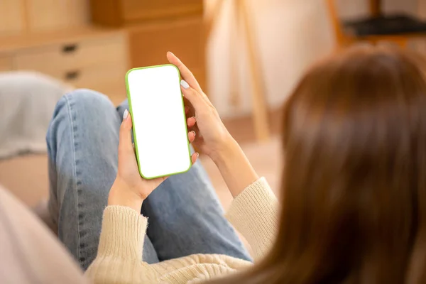 Young woman meeting in video conference with colleague on blank screen smartphone while wearing sweater and lying to working in holiday on sofa in cozy living room of christmas decoration