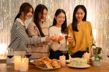 Genç, güzel bir kadın elinde havai fişek tutarken gece eğlenirken evde yeni yıl partisinin şenliklerine katılıyor..