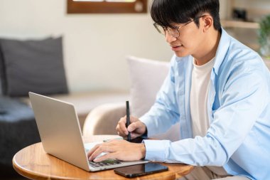 İş adamı rahat bir koltukta oturup yeni iş için düşünceli bir fikre sahipken evdeki dijital tablet üzerine iş projesiyle ilgili bilgi yazıp çalışmak için bilgisayarını kullanıyor..