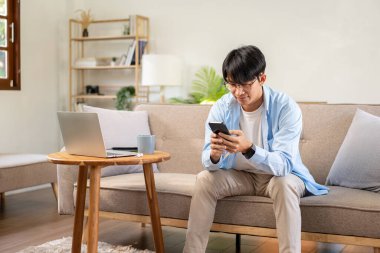 Gündelik iş adamı rahat bir koltukta oturup iş hakkında iş arkadaşlarıyla akıllı telefondan sohbet ederken evde oturma odasında çalışıyor..