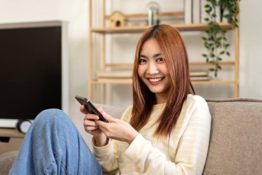 Genç kadın lezbiyen arkadaşlarıyla sohbet etmek için akıllı telefon kullanıyor ve evdeki büyük rahat kanepede dinlenmek için zaman harcarken internette veya eğlencede sörf yapıyor..