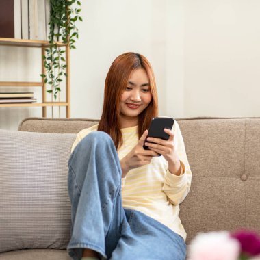 Genç kadın lezbiyen arkadaşlarıyla sohbet etmek için akıllı telefon kullanıyor ve evdeki büyük rahat kanepede dinlenmek için zaman harcarken internette veya eğlencede sörf yapıyor..