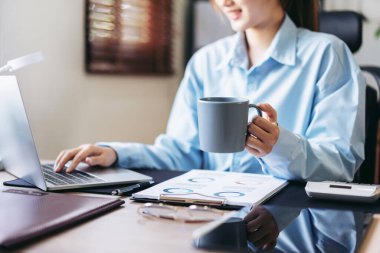 İş kadını, iş dünyasının muhasebesi ve sıcak çikolata içerken aynı zamanda bilgisayarla modern ofiste yeni iş projelerinin bilgilerini yazma ve yazma konusunda düşünceli..