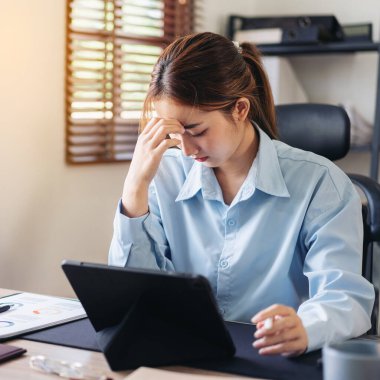 İş kadını, tabletten bilgi okurken baş ağrısı ve stresli hissediyor ve modern ofiste yeni bir iş projesi üzerinde çalışırken iş görüşmeleri hakkında düşünceli davranıyor..
