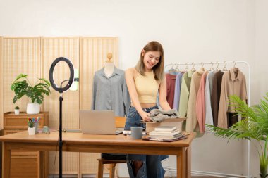 Kadın tasarımcı girişimci dizüstü bilgisayardan siparişleri kontrol ediyor ve giysi ürünlerini karton kutuya koyup eve nakliye için hazırlanıyor..