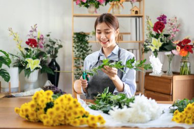 Çiçekçi dükkanında çiçek buketi yapmak ve yaratmak için beyaz kasımpatı sapını hazırlamak için makas kullanan önlüklü bir kadın..