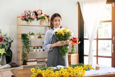 Çiçekçi dükkanında çiçek buketi hazırlarken ve dizayn ederken elinde kasımpatı tutarken gülümseyen ve eğlenen önlüklü kadın..